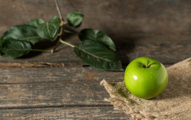 Green apple with leaves on burlap on wooden boards