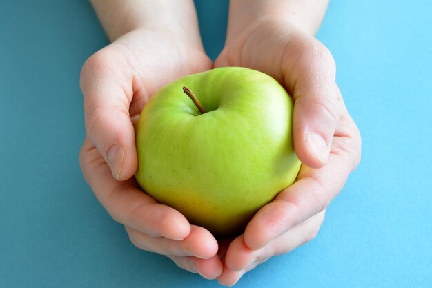 green apple in the woman's palms on the blue background isolated