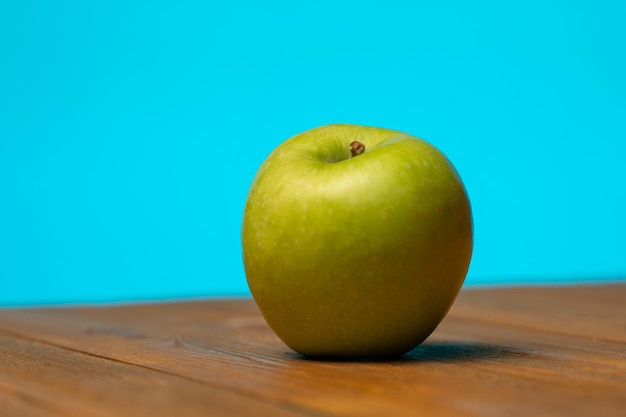 Green apple on a wooden table on a blue background