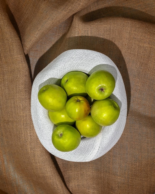 Green apples in a summer white hat on a natural textile background