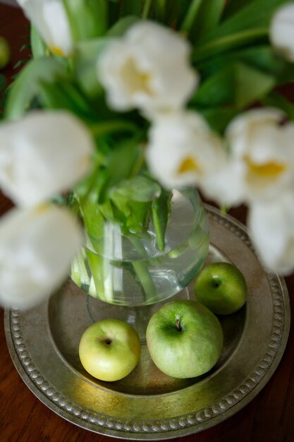 Green apples and tulips on round metal tray on brown wooden table