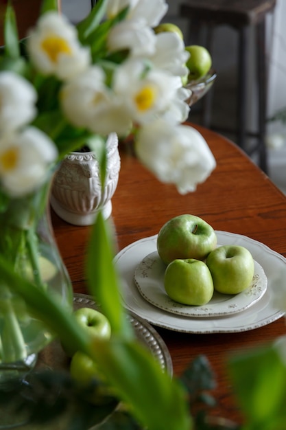 Green apples on white porcelain plate on brown wooden table