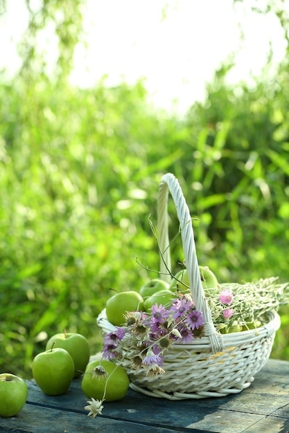 Green apples with bouquet of wildflowers on wooden table outdoors