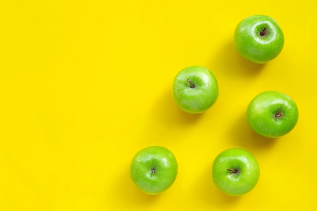 Green apples on yellow background. Copy space