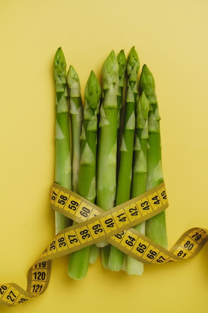 Photo green asparagus and measuring tape isolated on yellow