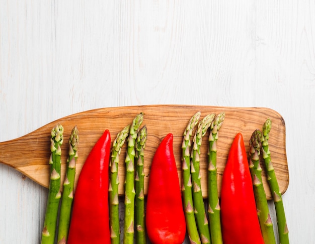 Green asparagus and red peppers on a cutting wooden board