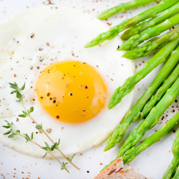 Green asparagus with fried egg and bread with butter on a white plate