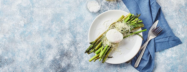 Green asparagus with poached egg and parmesan vegetarian breakfast served on white plate on light background