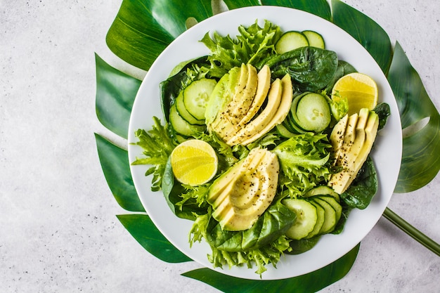 Green avocado and cucumber salad in white plate. Detox menu, vegan food, plant based diet.