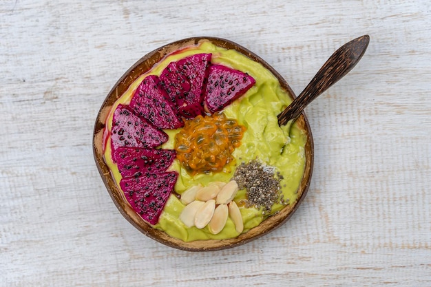 Green avocado smoothie in coconut bowl with dragon fruit passion fruit almond flakes coconut chips and chia seeds for breakfast close up The concept of healthy eating superfood Bali Indonesia