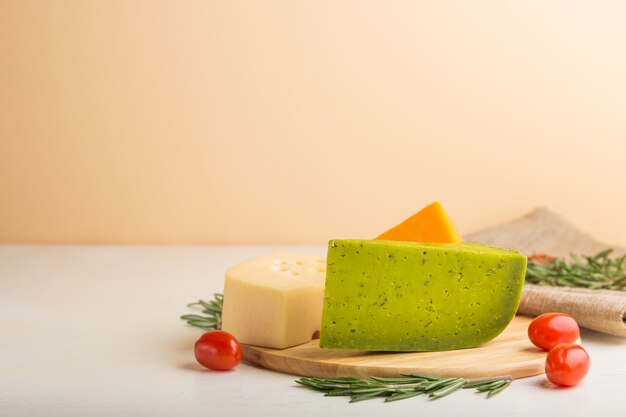 Green basil cheese and various types of cheese with rosemary and tomatoes on wooden board on a white wooden background. Side view, copy space.