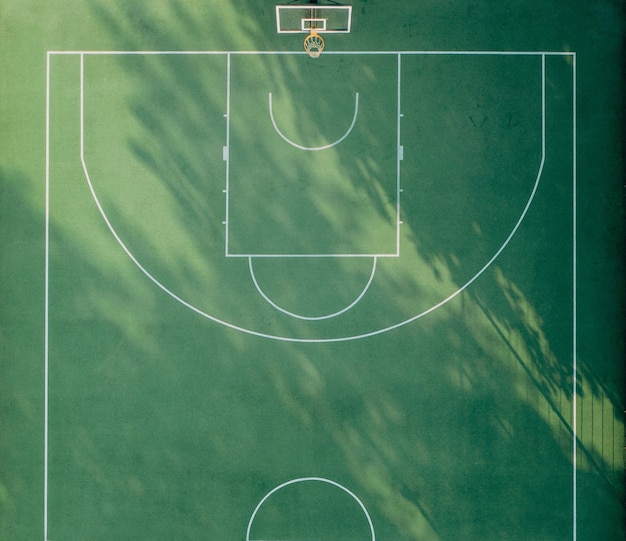 Green basketball playground with white markings and morning shadows top view