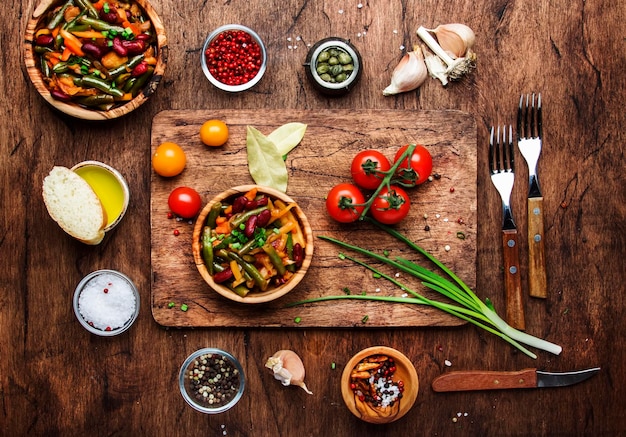 Green beans with roots vegetables mushrooms spices and tomatoes vegan bowls Food cooking background vintage wooden rustic table View from above