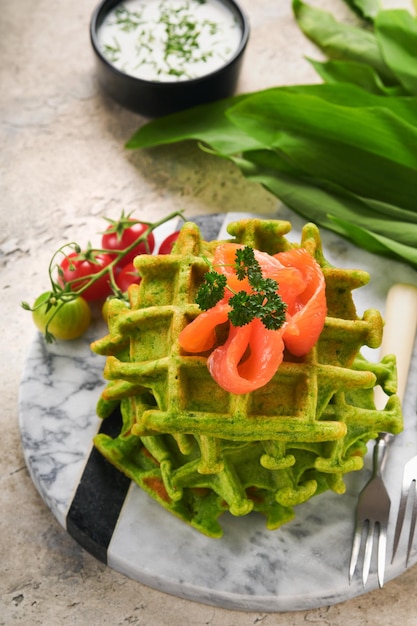 Green Belgian waffles Spinach or wild garlic or pesto waffles with red salmon and cream sauce on grey concrete table background Delicious breakfast snack brunch Mock up Selective focus