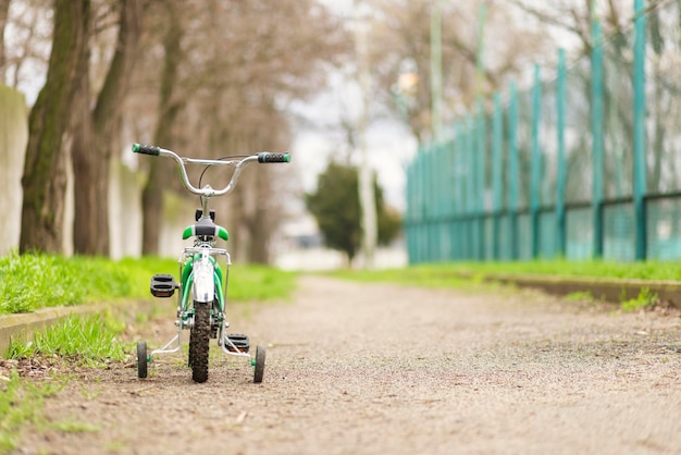 A green bicycle for children with additional wheels at road in park