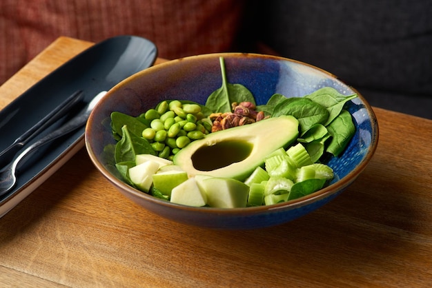 Green bowl of healthy food vegan bowl with avocado apple and green vegetables on a wooden background