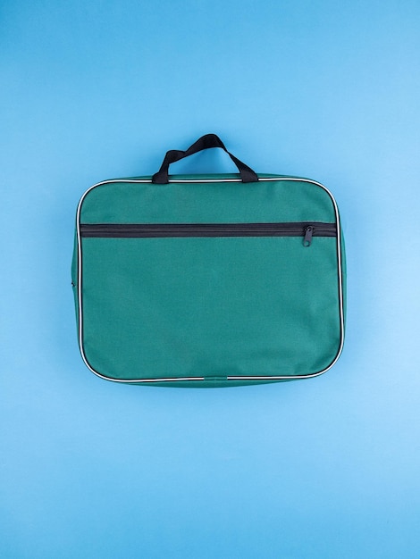 Green briefcase folder for documents and school items on a bright blue table next to stationery