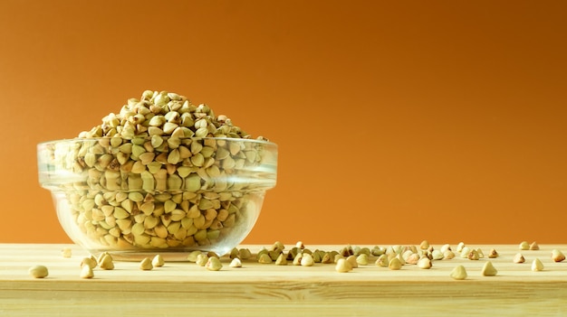 Green buckwheat in a glass transparent bowl on a brown background.