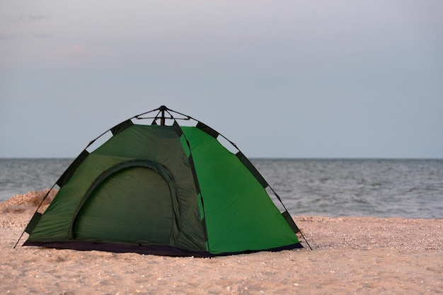 Green camping tent on sandy beach against sea background Camping by the sea