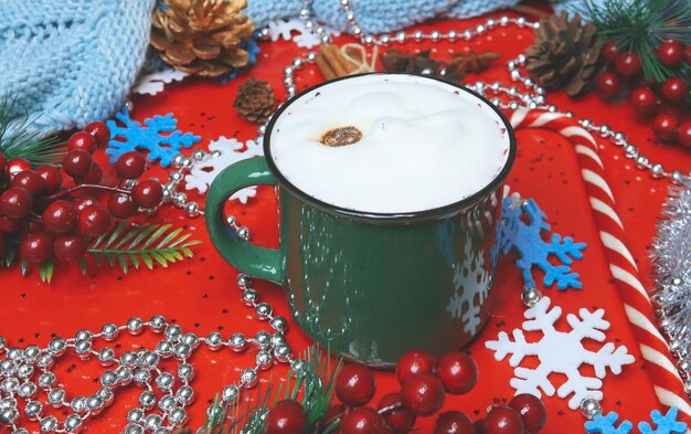 Green cappuccino mug with Christmas decorations on a red background.