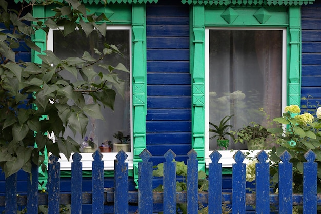 Green carved platband windows with curtains of old traditional russian painted blue wooden house