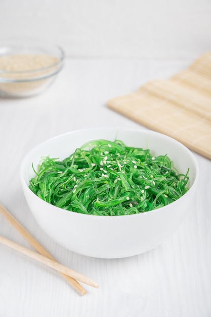 Green chuka wakame seaweed salad with sesame seeds served in bowl with bamboo chopsticks on table