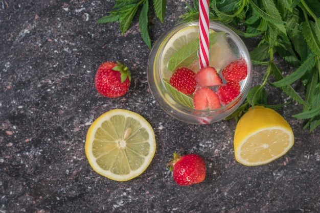 Green cocktail tube in a glass of ice water with lemon mint and berries