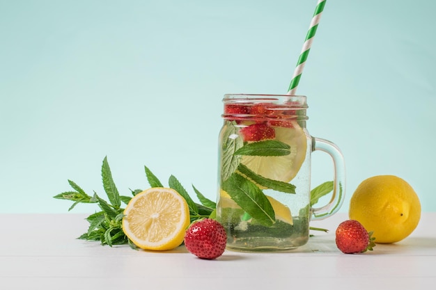 Green cocktail tube in a mug with cold water berries and lemon