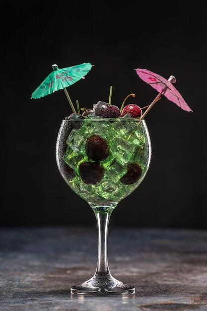 Green cocktail with ice and cherries in a glass decorated with umbrellas