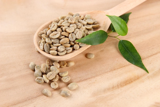 Green coffee beans in spoon and leaves on wooden background