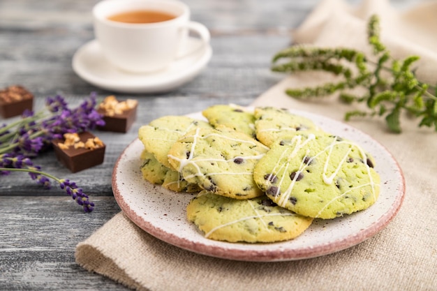 Green cookies with chocolate and mint with cup of green tea on gray wooden background side view close up selective focus