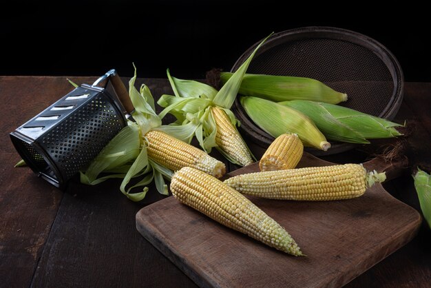 Green corn arranged on a rustic wooden table with old accessories on black