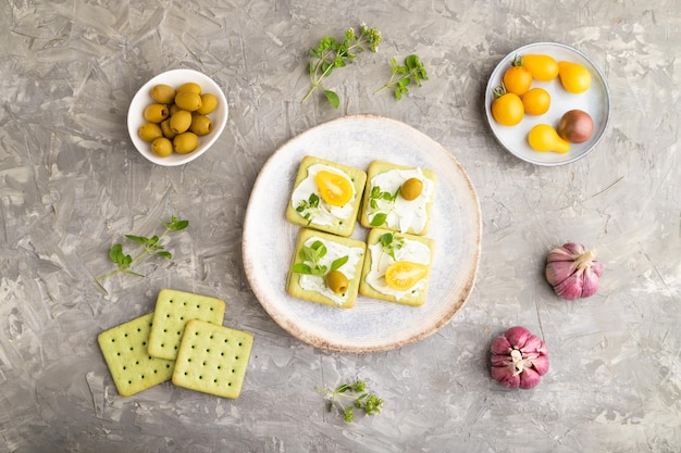 Green cracker sandwiches with cream cheese and tomatoes on gray concrete background top view close up