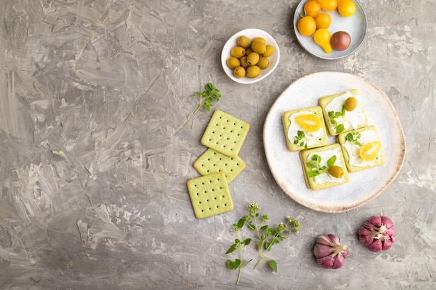 Green cracker sandwiches with cream cheese and tomatoes on gray concrete background top view