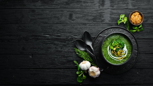 Green cream of broccoli soup and pumpkin seeds in black bowl Top view Free space for your text Rustic style