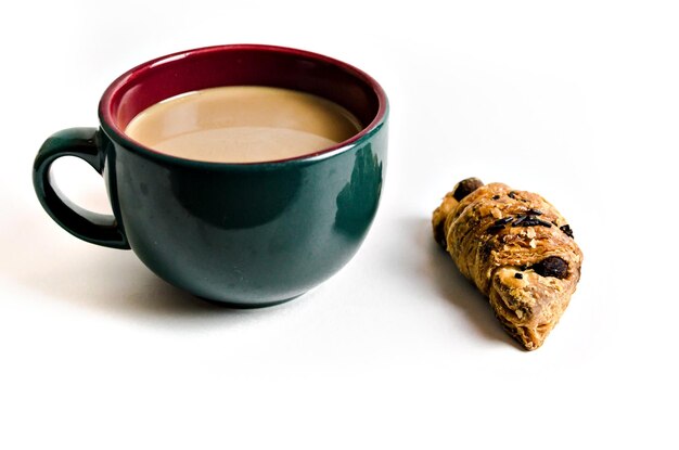 Green cup of coffee with milk and croissant on the table in white background. Breakfast.