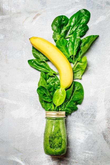 Green detox smoothies made from spinach leaves in a glass bottle top view food background