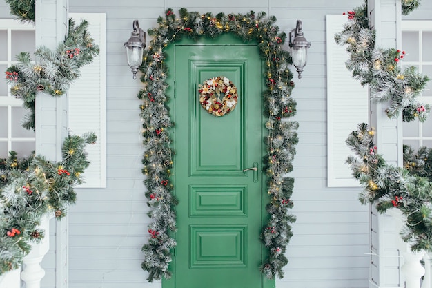 Green door entrance to the house. Christmas festive deco decorated with Christmas tree branches