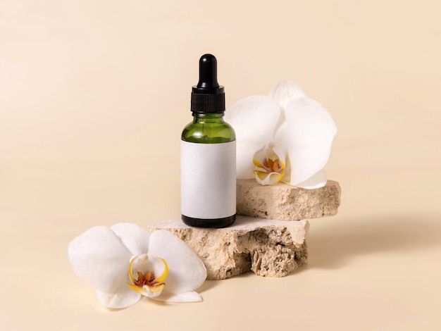 Green dropper glass bottle near white orchid flowers on light yellow Mockup Skincare product