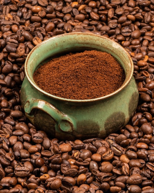 A green earthenware cup with ground coffee in the middle of many coffee beans Awakening Tonic drink 