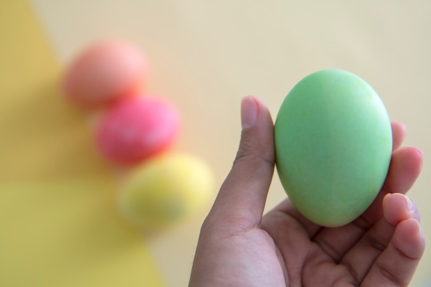 green easter egg in hand with colorful pastel background. 