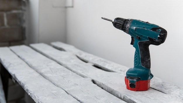 A green electric screwdriver stands on a white wooden boards close to white wall. Do-it-yourself