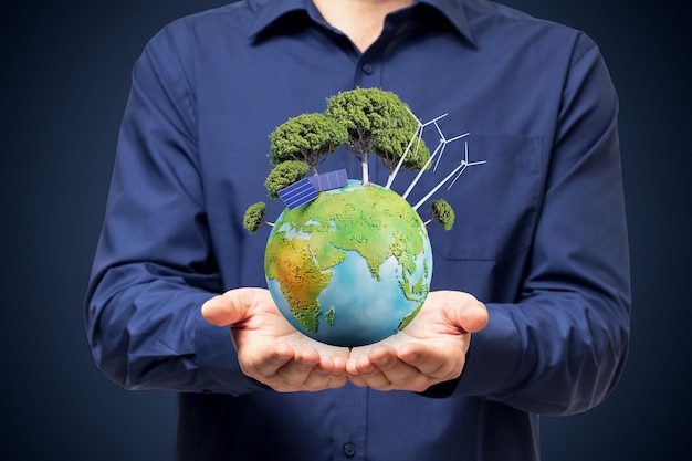 Green energy and save the environment concept with small earth planet miniature with trees solar panels and windmills in man hands on background