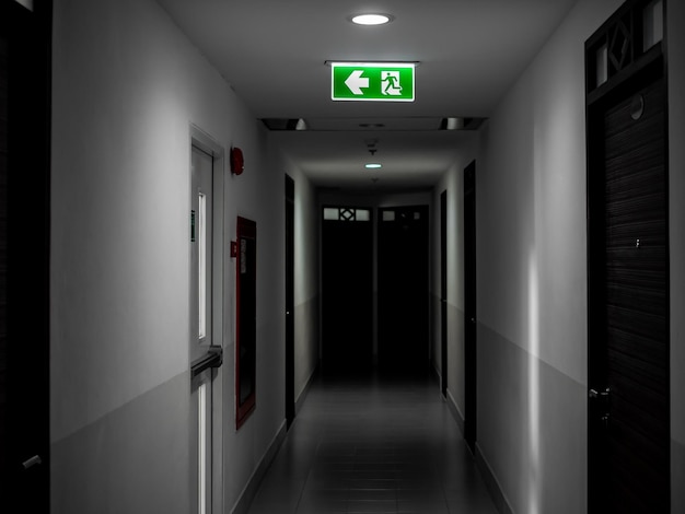 Green exit fire sign hanging on ceiling on dark mysterious corridor in building near fire exit door