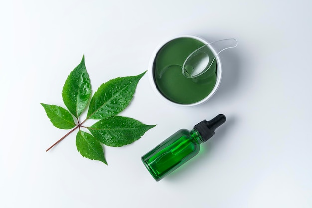 A green face serum or essential oil made of grapes and eye antiaging patches lying on a white background