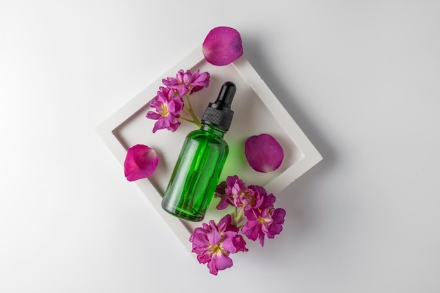 A green face serum or oil with flower extract lying between the petals product marketing mockup A concept of hair care in a salon or at home