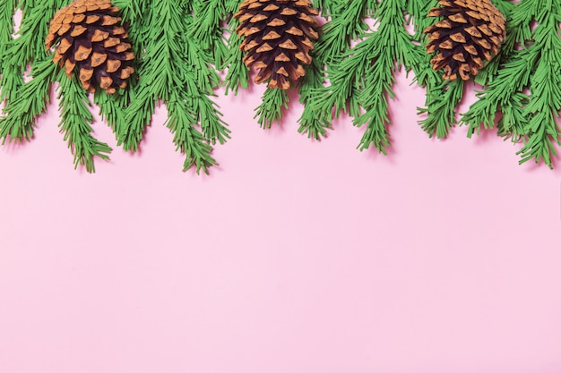 Green foam Christmas tree branch border with cones on the pink background flat lay