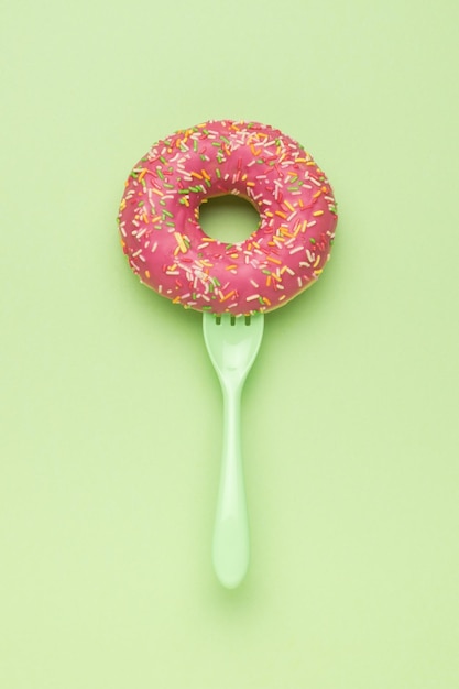 A green fork in a red donut on a green background The minimal concept of popular baking