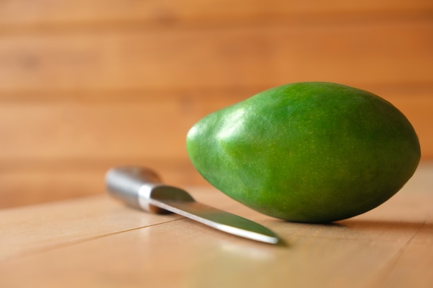 Green fresh mango tropical whole fruit on natural brown wooden table background knife healthy tasty ...