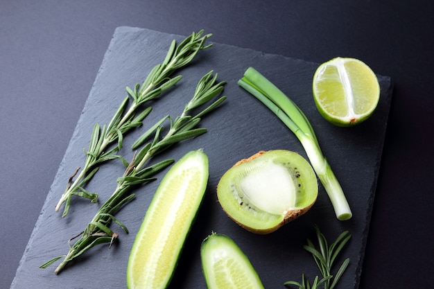 Green fruits and vegetables on dark slate board. Concept of natural green products. Avocado, kiwi, lime and apple on dark background. Rosemary, dill and chives on stone board